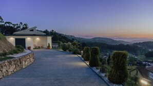 A modern house with a paved driveway, a stone retaining wall, and a view of the surrounding hills. - Villa Cantinho da Cavadinha (Burgo)