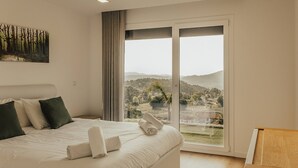 A bedroom with a large bed, a view of the countryside, and a wooden side table. - Villa Cantinho da Cavadinha (Burgo)