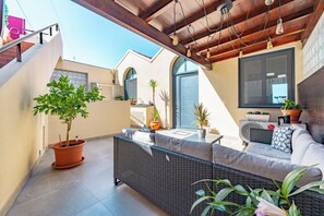 Une terrasse extérieure moderne, dotée de meubles en osier, de plantes en pot et d’un plafond en bois.