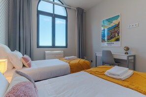 Une chambre d’hôtel avec deux lits, un bureau, une chaise, une lampe et une affiche de Madère, au Portugal.