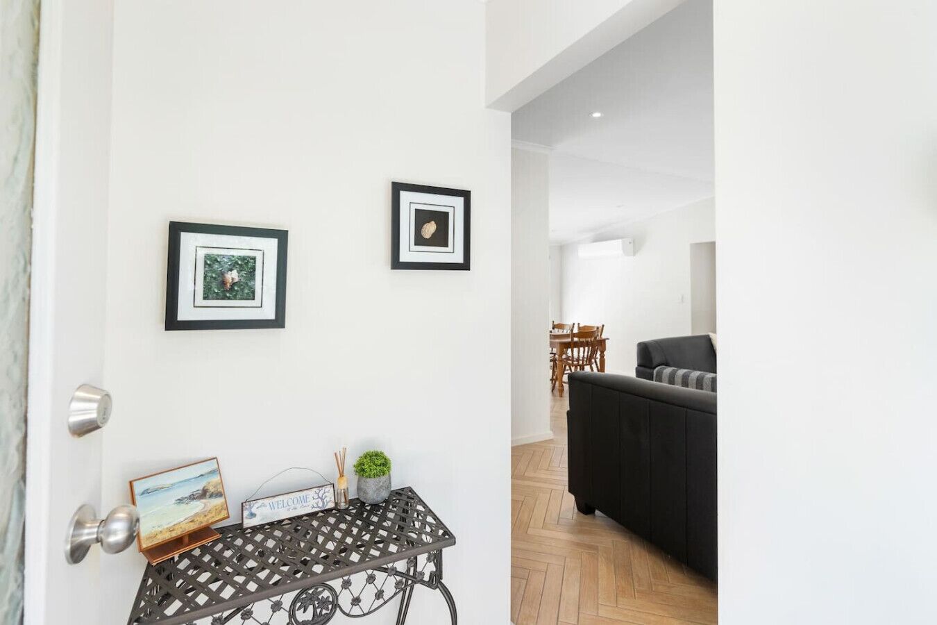 A modern living room with a black sofa, a small table with a welcome sign, and two framed pictures on the wall.