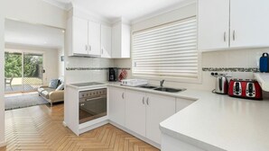 Una cocina moderna con armarios blancos, horno empotrado, pileta y ventana con persianas.