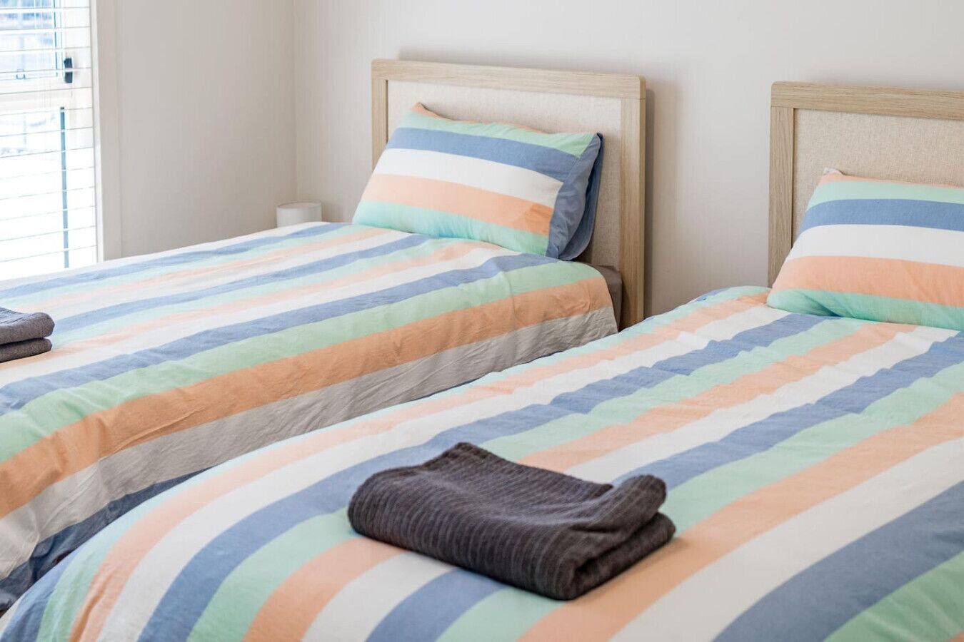 Two single beds with striped bedding in a room with a wooden headboard and a plain wall.