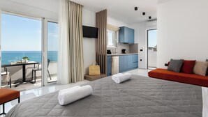 Ein modernes Hotelzimmer mit einem großen Bett, einem Balkon mit Meerblick, einer Küchenzeile und einer Sitzecke mit einer Couch.