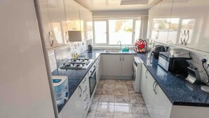 A modern kitchen with white cabinets, a granite countertop, and a window providing natural light. - Cozy House in Central Andover (Parking, 65” TV) (Andover)