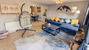 A living room with a blue sofa, a hanging chair, a coffee table, and a world map on the wall. - Cozy House in Central Andover (Parking, 65” TV) (Andover)