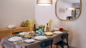 A dining area with a table set for four, featuring a patterned tablecloth, plates, cutlery, and various decorative items like vases and bottles. - Villaelena in Marittima (Marittima)