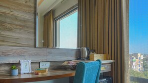 A modern hotel room with a wooden desk, a chair, a large mirror, and a city view. - A K CONTINENTAL (Amritsar)