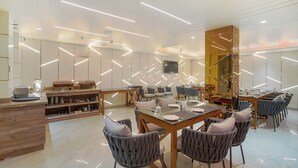 A modern dining area with a wooden table, grey upholstered chairs, and a glass partition wall. - A K CONTINENTAL (Amritsar)