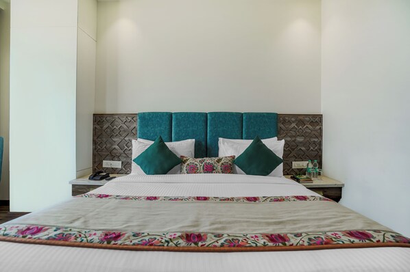 A neatly made bed with floral bedspread, a headboard with a geometric pattern, and two bedside tables with water bottles and a phone.