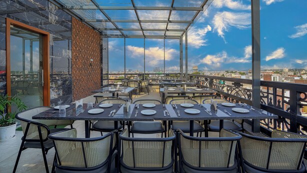 A rooftop restaurant with a glass enclosure, tables set for dining, and a city view. - A K CONTINENTAL (Amritsar)