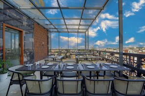 A rooftop restaurant with a glass enclosure, tables set for dining, and a city view.