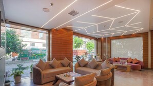 A modern lobby with leather sofas, a coffee table, and large windows offering a view of the street. - A K CONTINENTAL (Amritsar)