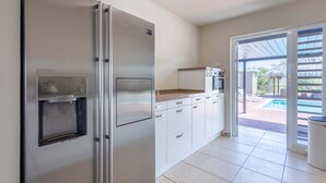 A modern kitchen with a built-in water dispenser, white cabinets, and a view of a swimming pool through glass doors. - Ser na Private Retreat (St. Marie)