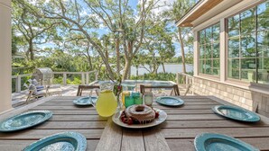 A wooden deck with a table set for a meal, surrounded by large windows and trees. - Immaculate new Rhett's Bluff property (Kiawah Island)
