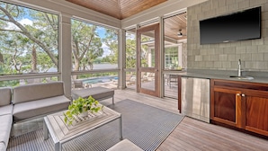 A modern outdoor living area with a wooden ceiling, a built-in TV, and a view of a pool and trees. - Immaculate new Rhett's Bluff property (Kiawah Island)