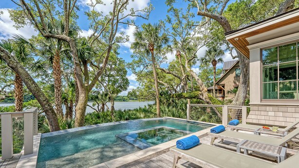A private pool with lounge chairs and a wooden deck, surrounded by trees and a view of a lake. - Immaculate new Rhett's Bluff property (Kiawah Island)