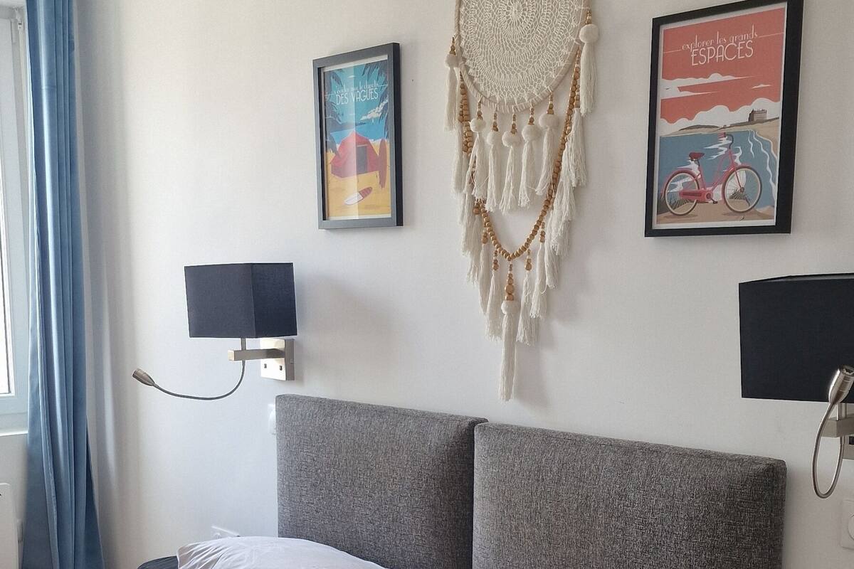 A neatly made bed with a patterned bedspread, a grey headboard, and two wall-mounted speakers.