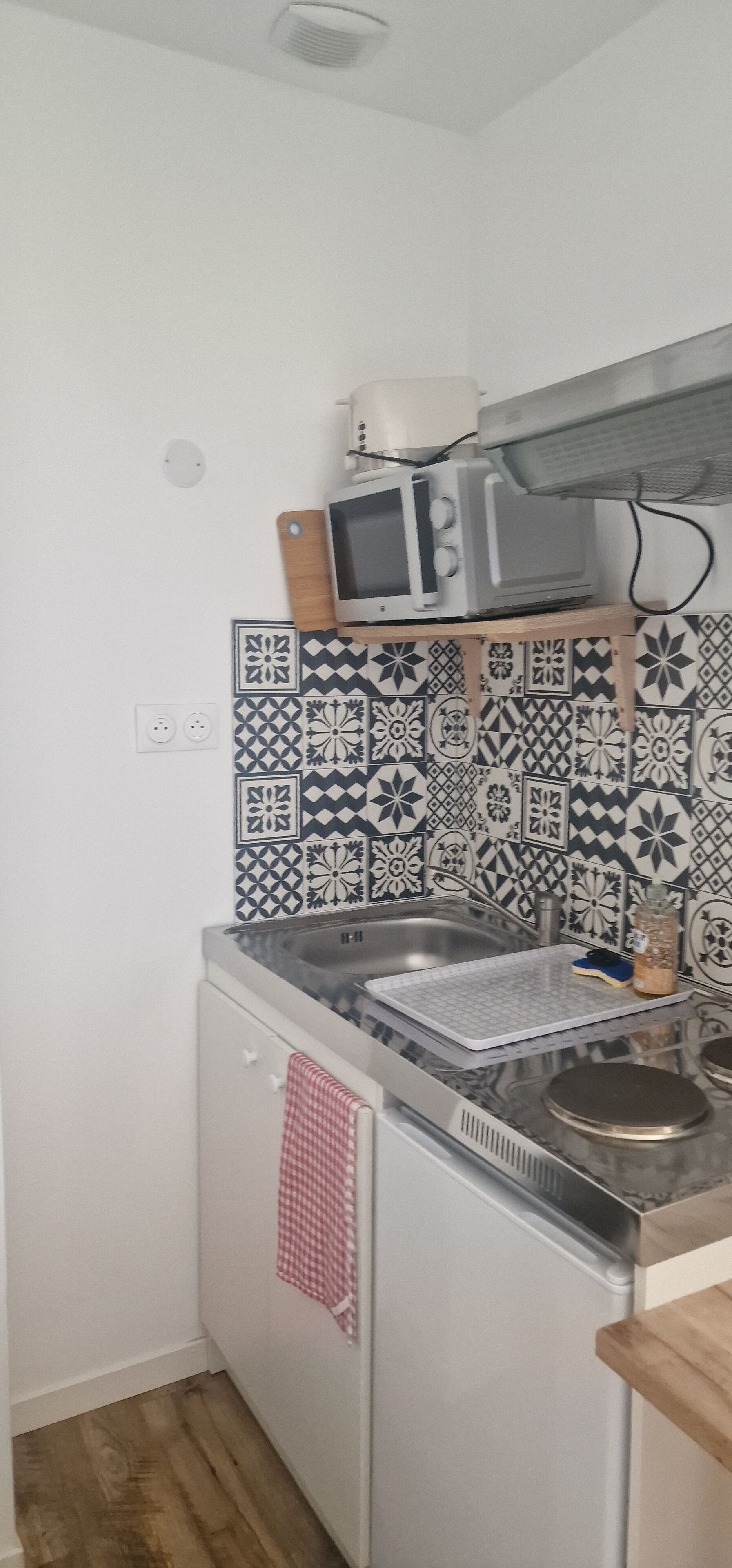 Een compacte keuken met een magnetron, een klein spoelgedeelte en een vaatwasser. De spatwand is voorzien van zwart-wit betegeling.