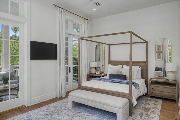 Une chambre à coucher avec un lit à baldaquin, un banc, une table de chevet, un miroir et un téléviseur fixé au mur.