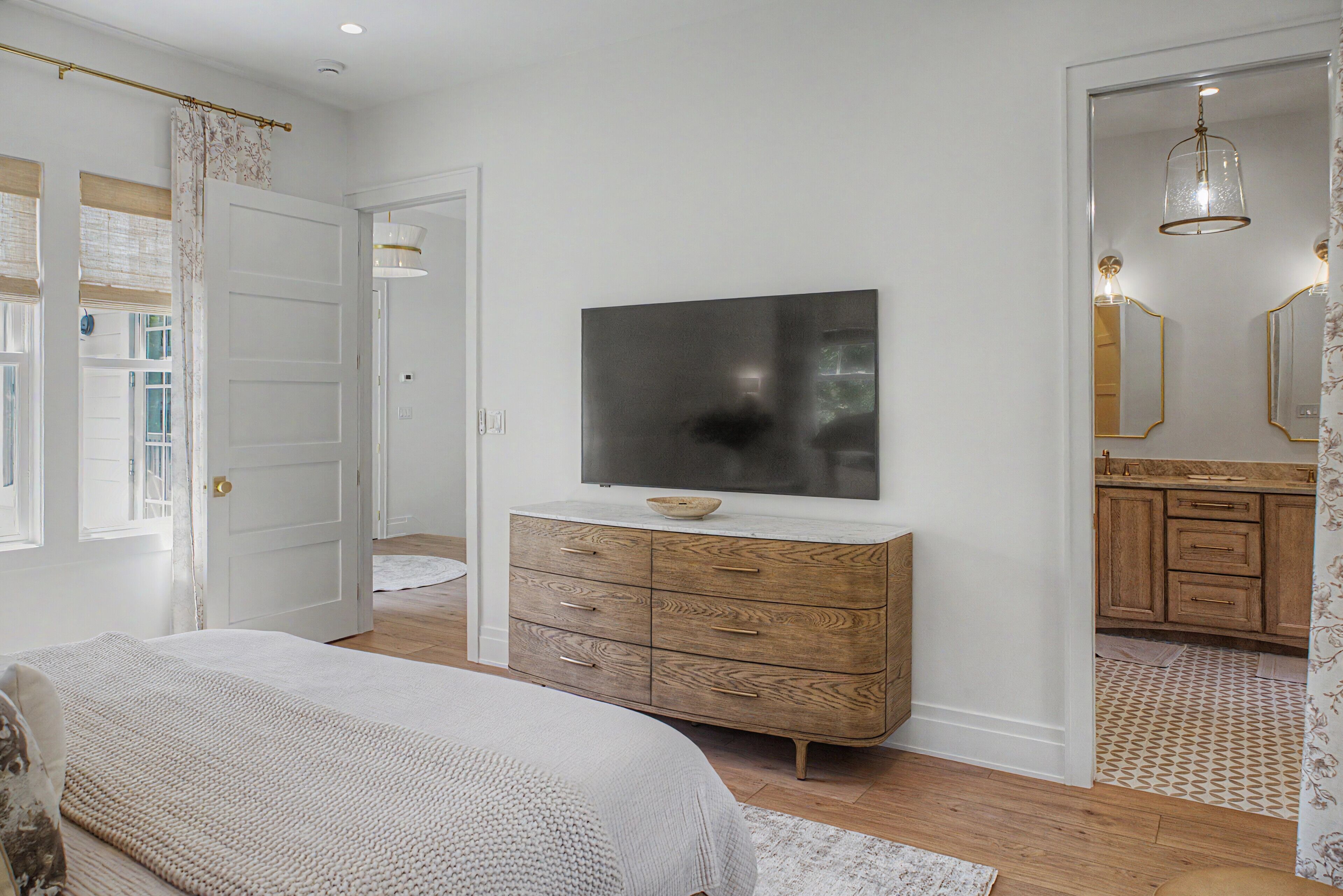 A bedroom with a bed, a dresser, a television, and a bathroom visible through an open door.