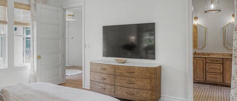 A bedroom with a bed, a dresser, a television, and a bathroom visible through an open door.