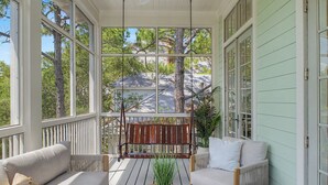 A covered porch with a swing, a cushioned sofa, a round table, and a potted plant. - Stunning Down-to-the-Studs Remodel  – Across from Camp WaterColor (Santa Rosa Beach)