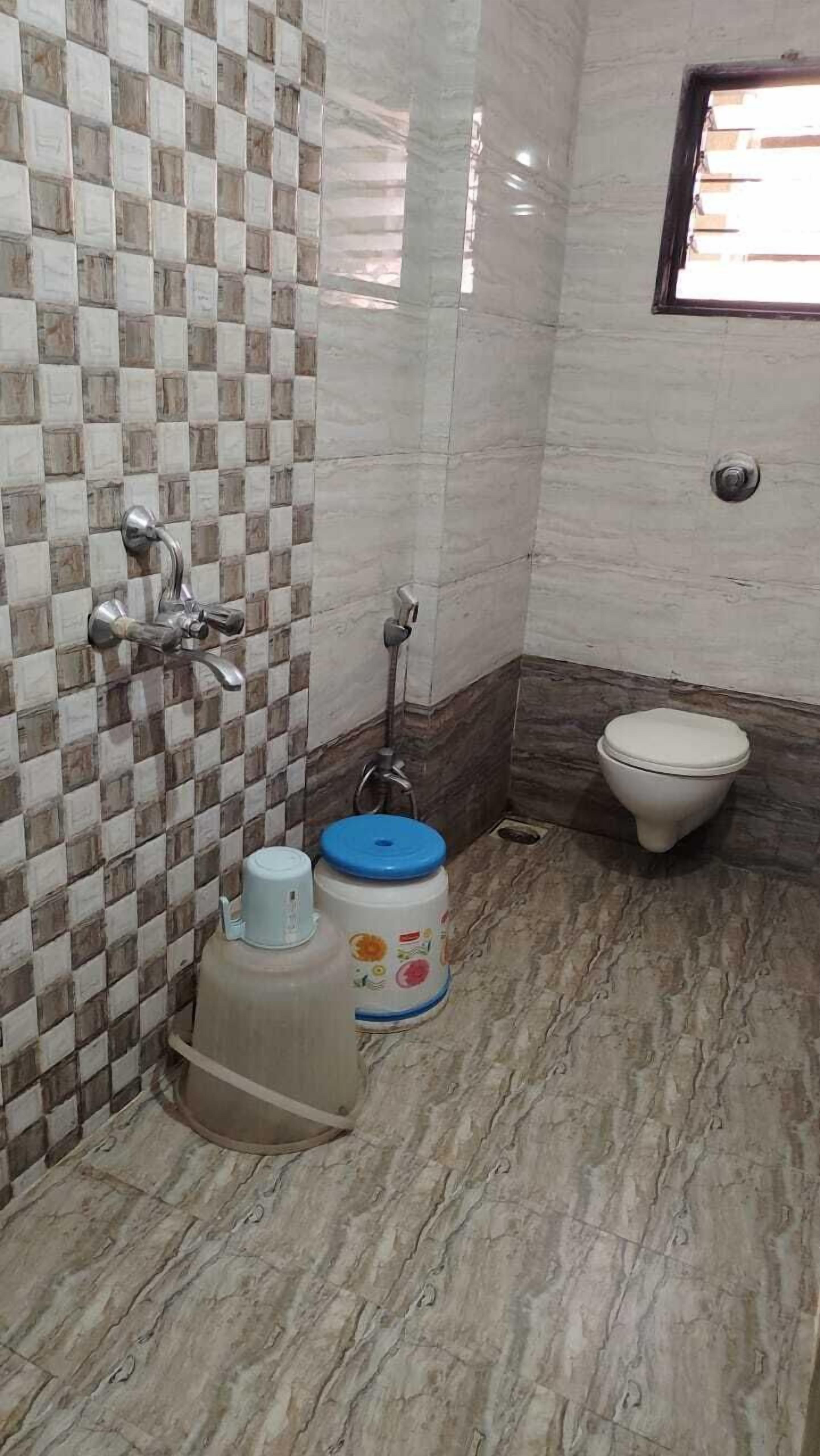 A bathroom with a tiled floor, a toilet, a shower, and a sink.