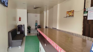 Un área de recepción con mostrador, un sofá, dispensador de agua, un reloj y un extintor.