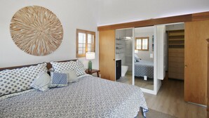 A bedroom with a bed, a large wall art piece, a mirror, and a sliding door leading to a bathroom.