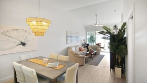 A modern living room with a dining area, featuring a chandelier, artwork, and a large plant.