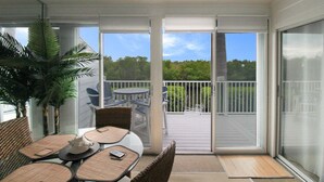 A balcony with a table and chairs, a potted plant, and a view of a deck and trees.
