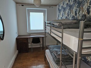 Un dormitorio con literas, un escritorio, una silla, un radiador y una ventana.