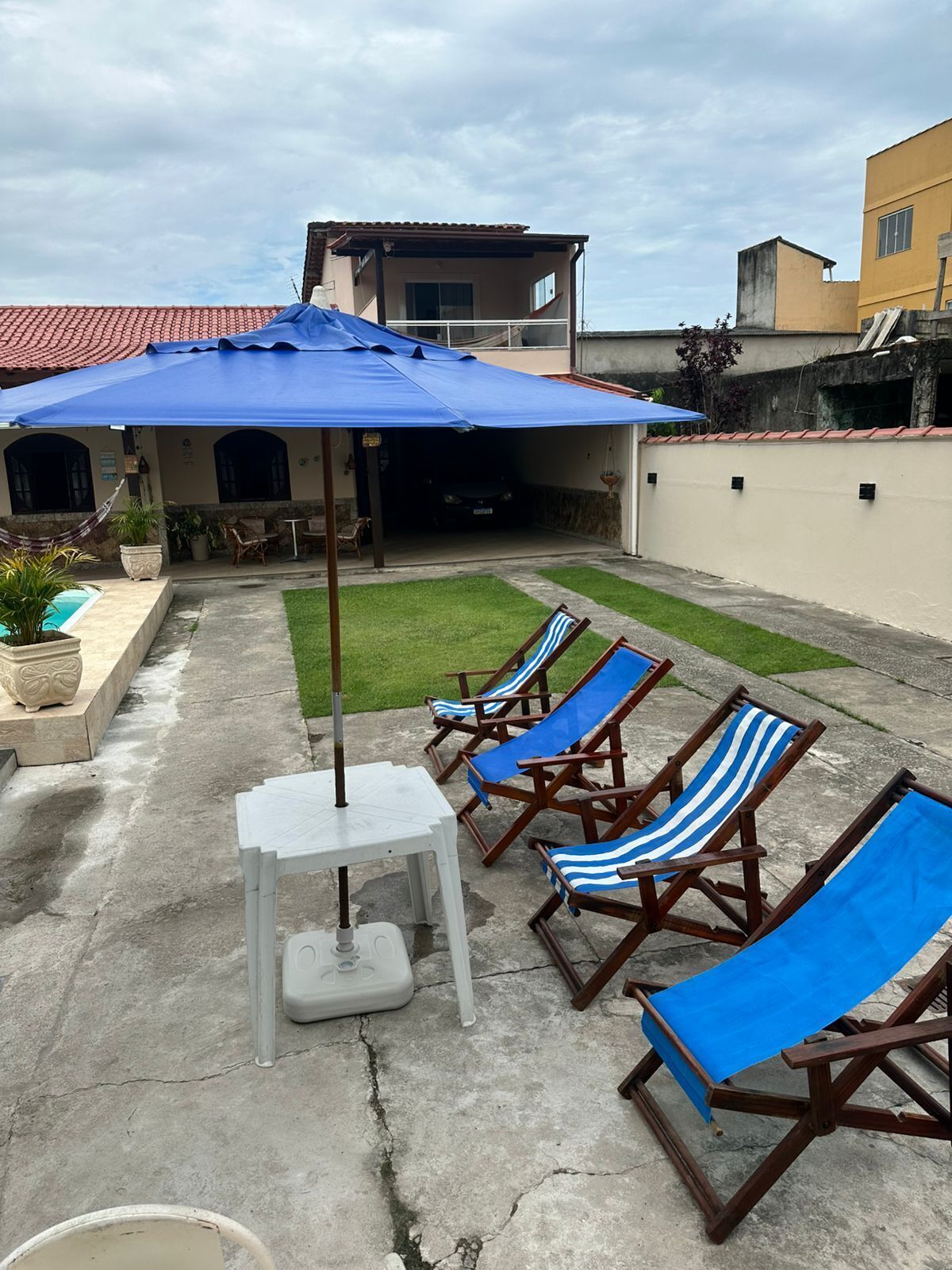 A patio with lounge chairs, a table, and a blue umbrella.
