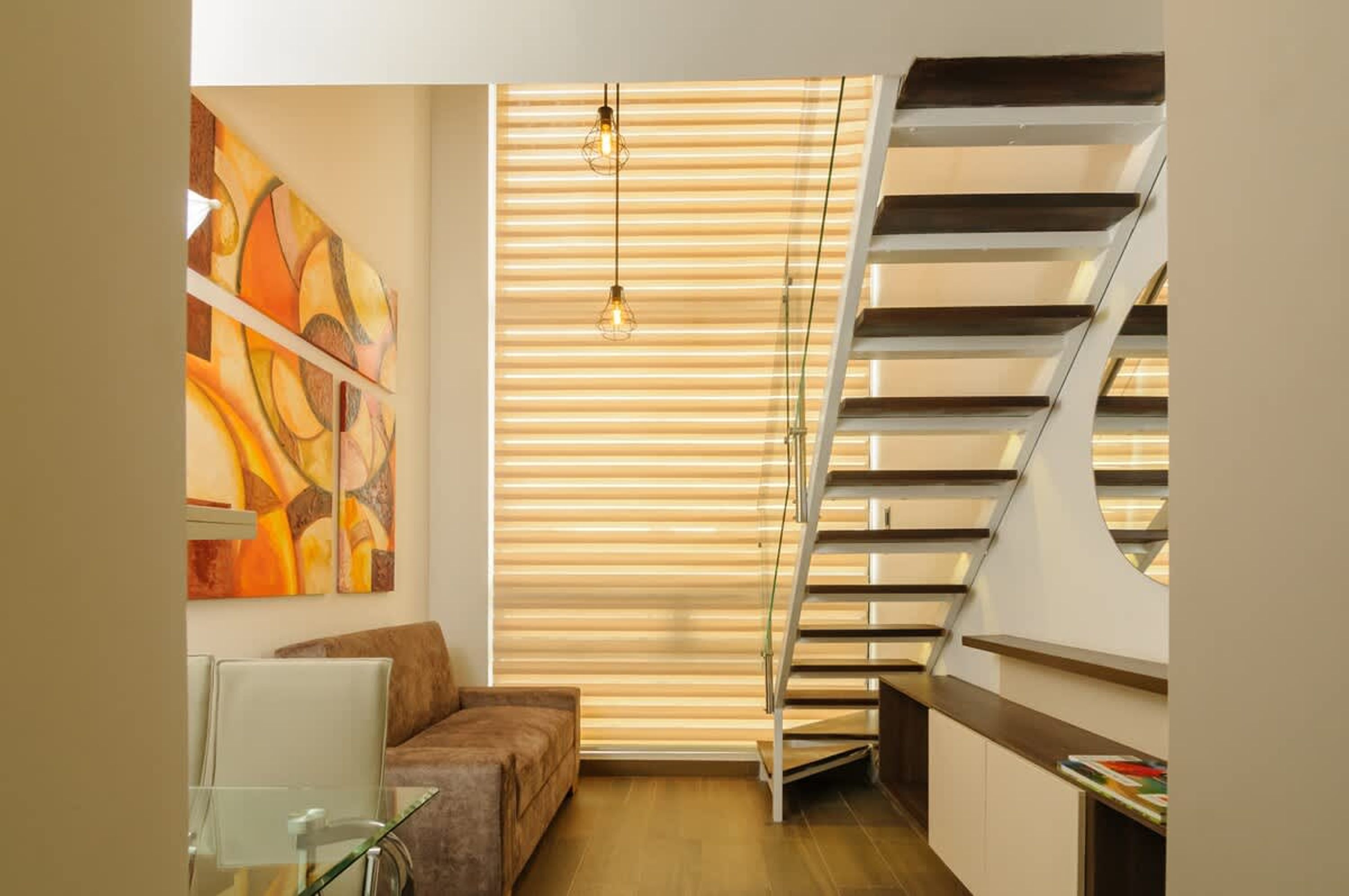 Un intérieur moderne avec un escalier, des œuvres d’art abstraites accrochées au mur et une table en verre.