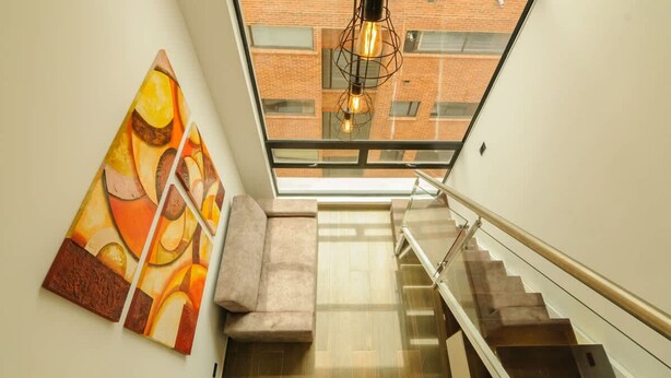 A modern staircase with glass railings, a view of a brick building through a skylight, and abstract art on the wall. - NOK Spacious Duplex in Parque 93 (Bogotá)