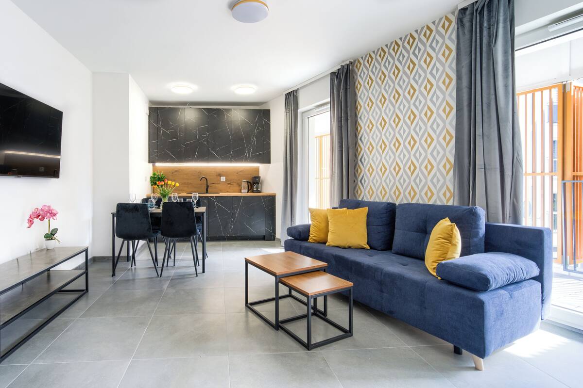 A modern living room with a blue sofa, a wooden coffee table, and a dining area with a black table and chairs.