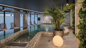 Un área interior de piscina moderna con sillones de descanso, una planta grande en maceta y un suelo con mosaicos.