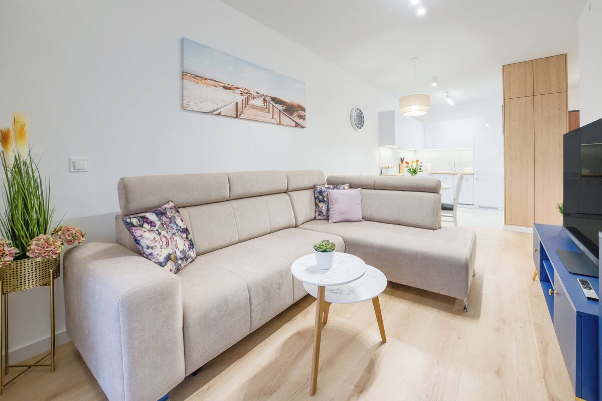 A modern living room with a beige sofa, a small round table, and a TV stand.