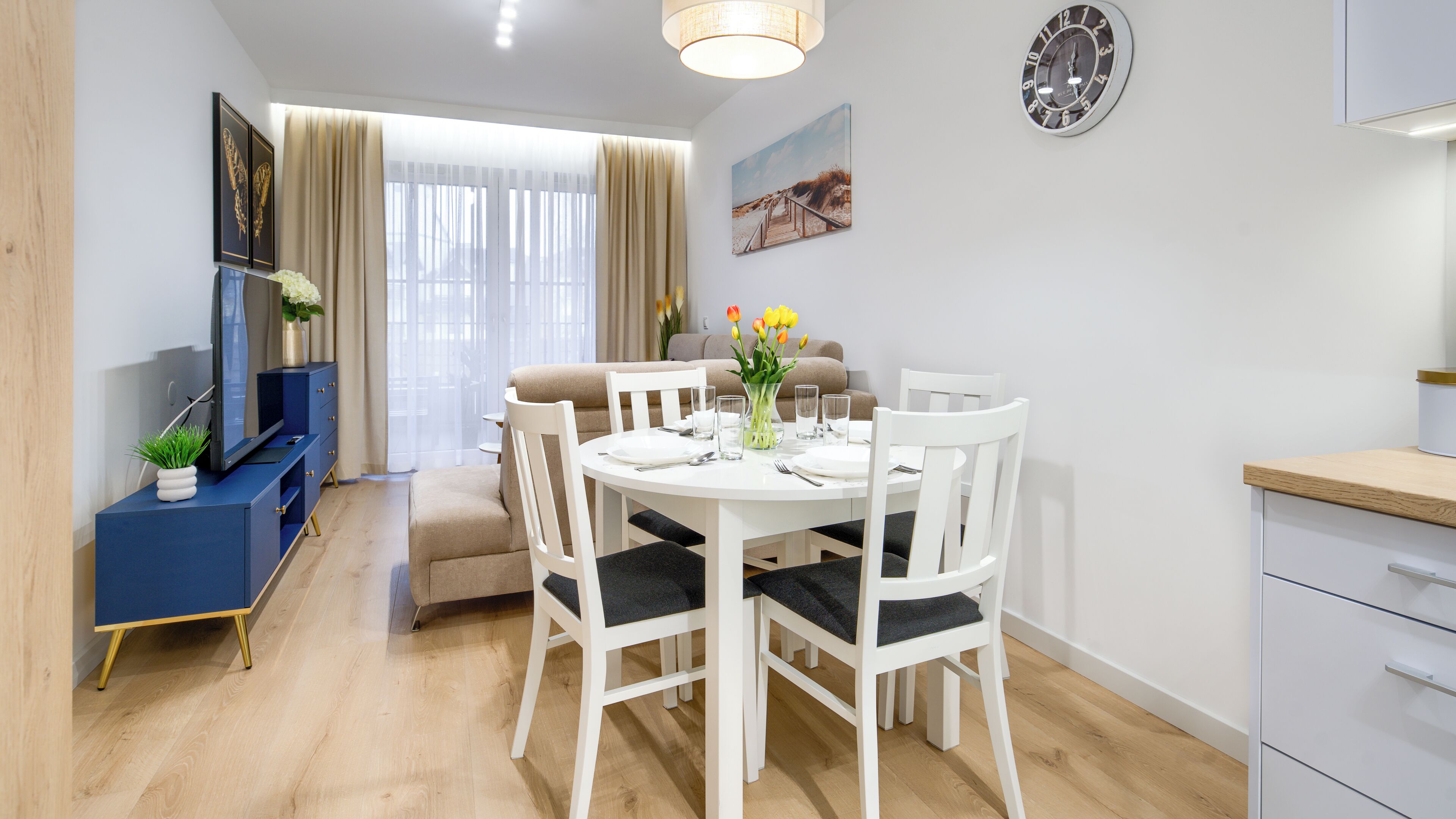 A modern dining area with a round table, white chairs, and a vase of flowers.