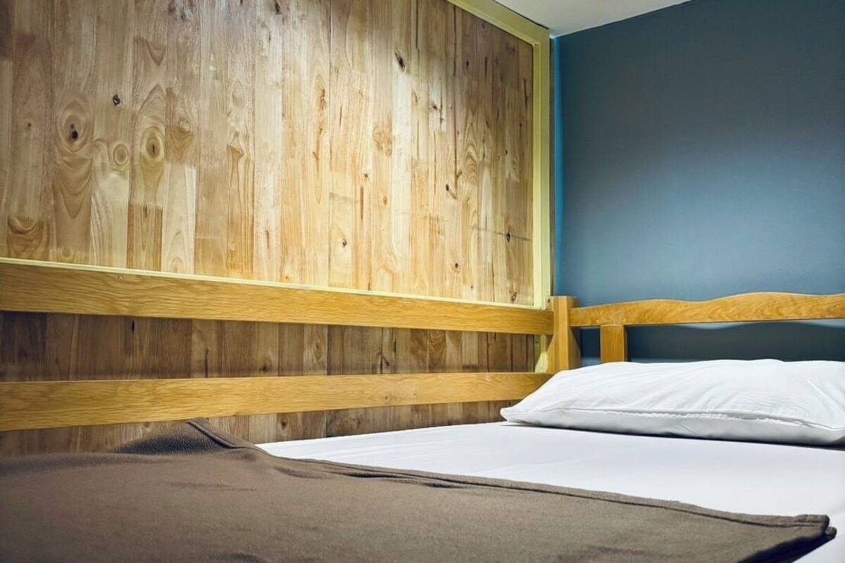 A single bed with wooden headboard and footboard, white bedding, and a ceiling light.