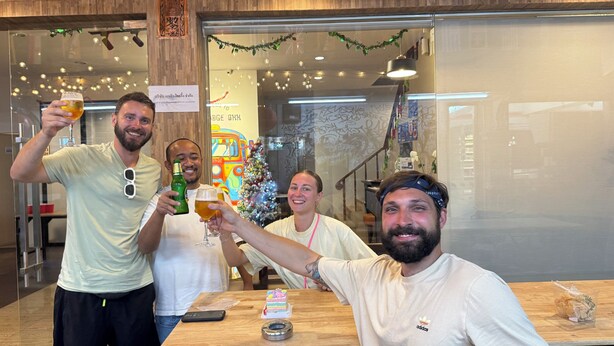 Un grupo de personas brindando con bebidas en una mesa con un pastel y un teléfono.