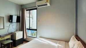 Una habitación de hotel con una cama grande, un escritorio con ordenador, un televisor de pantalla plana y un equipo de aire acondicionado.