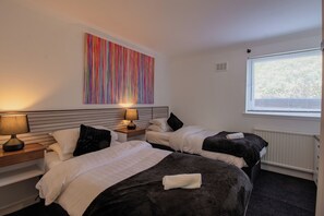 A hotel room with two beds, a large colorful artwork on the wall, a window with blinds, and a radiator.