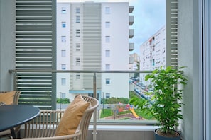 Enjoy the view of the surrounding neighborhood from this balcony, featuring a potted plant and a comfortable wicker chair.