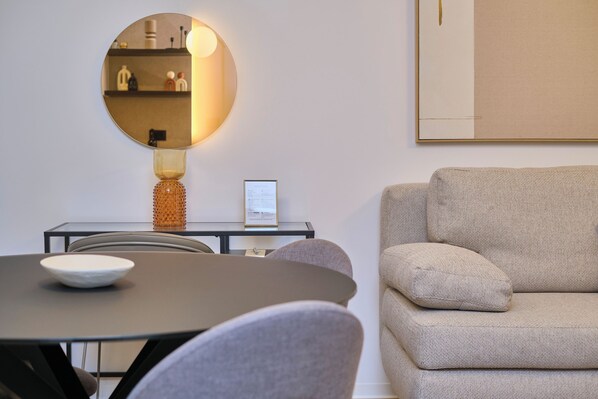 A modern living room with a round mirror, a sofa, and a dining table with chairs. - Splitful Apartment (Split)
