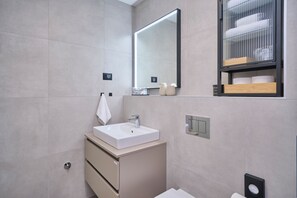 A modern bathroom with a white sink, a mirror, and a shelf with towels.