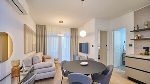 Ett modernt vardagsrum med ett runt matbord, grå soffor och en platt-TV.