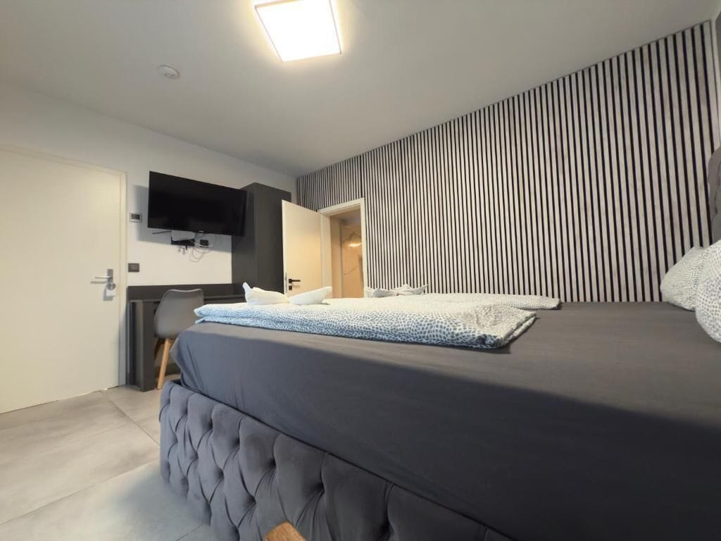 A modern bedroom with a large bed, a flat-screen TV mounted on the wall, and a striped wall design.