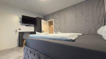A modern bedroom with a large bed, a flat-screen TV mounted on the wall, and a striped wall design.